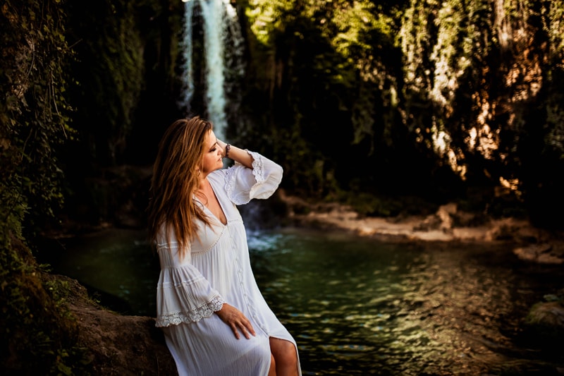 London Family Photographer, a woman in a white dress sits relaxing near a lush green waterfall setting