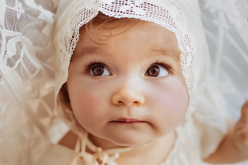 London Family Photographer, a baby girl's eyes look off curiously, she is dressed in all white