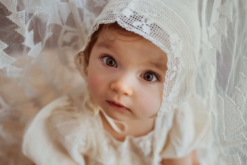 London Family Photographer, a baby is adorned in all white curious at her surroundings
