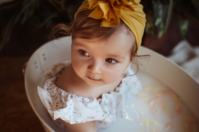 London Family Photographer, little baby girl sits in a large metal bucket in a flower and milk bath