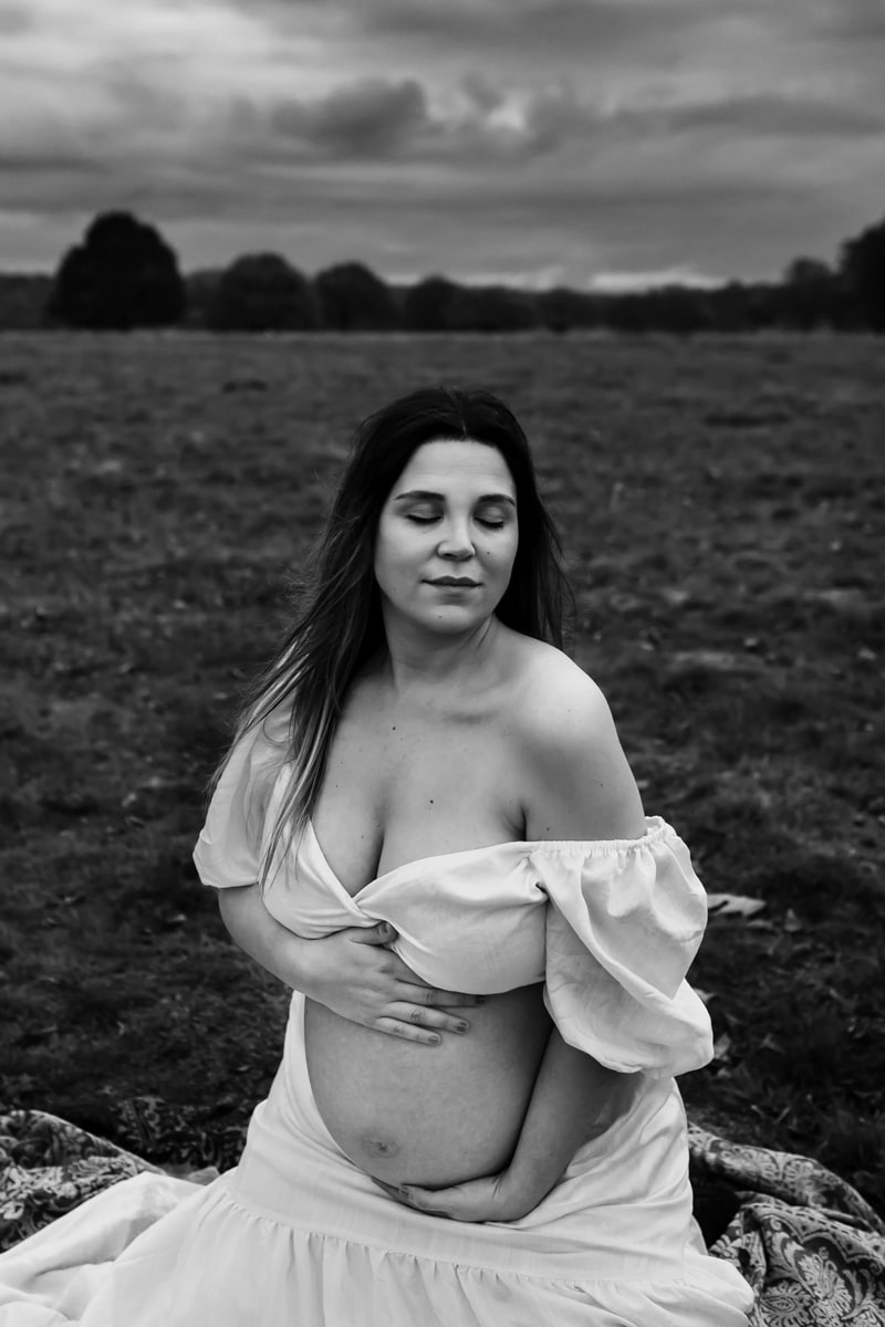 London Family Photographer, pregnant woman sits outdoors in the grass happy