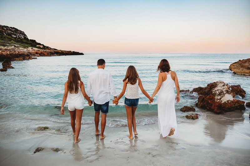 London Family Photographer, a family of four with two daughters walk toward the ocean holding hands